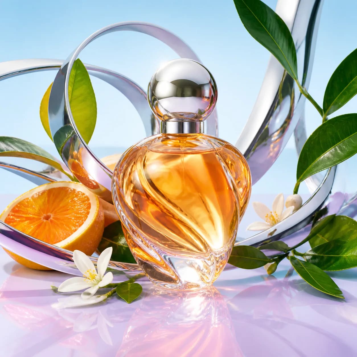 Source reference: An unlabeled citrus glass perfume bottle framed by chrome ribbons and green leaves